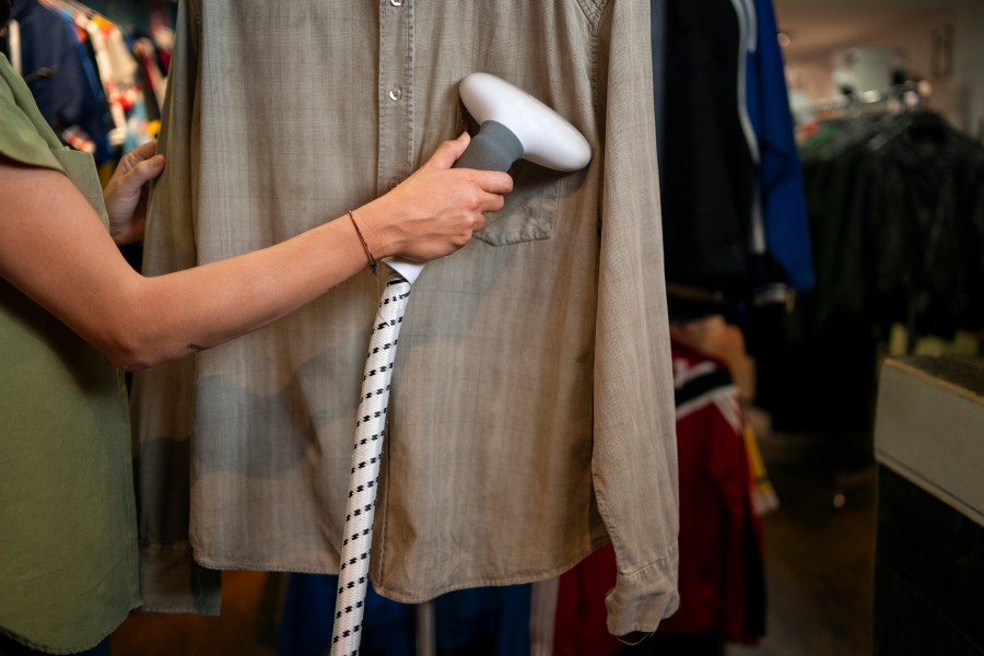 Dry cleaning service provider steaming a beige shirt with a handheld garment steamer